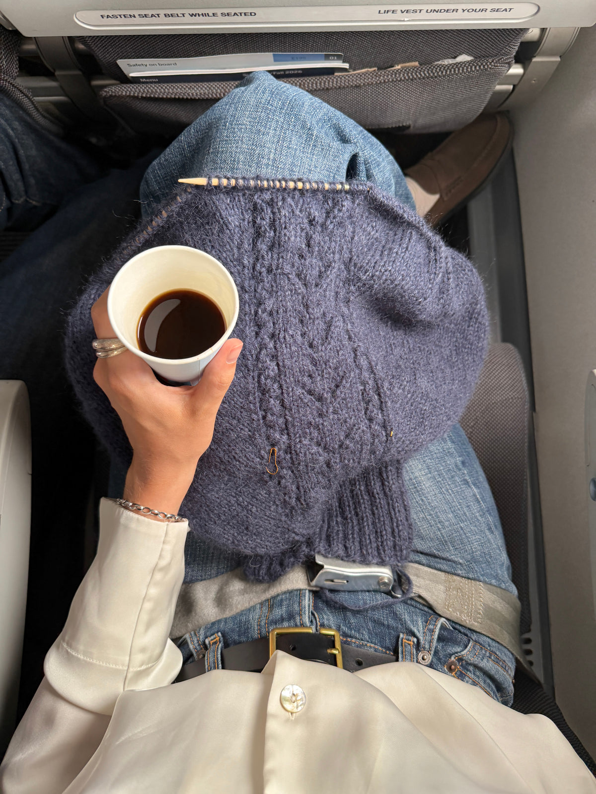 A navy Jolie Sweater in progress on the needles, with a cup of coffee, on a plane